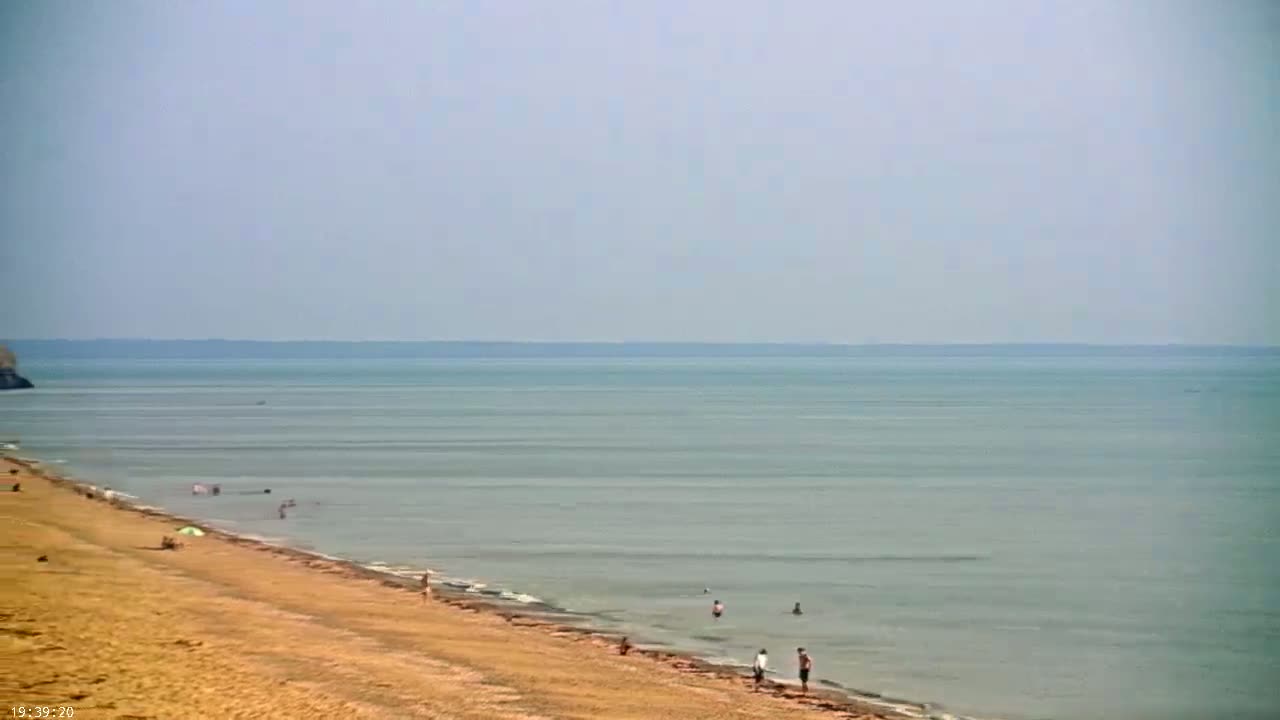 A sandy beach slopes down to a calm, light-grey sea under a hazy sky.