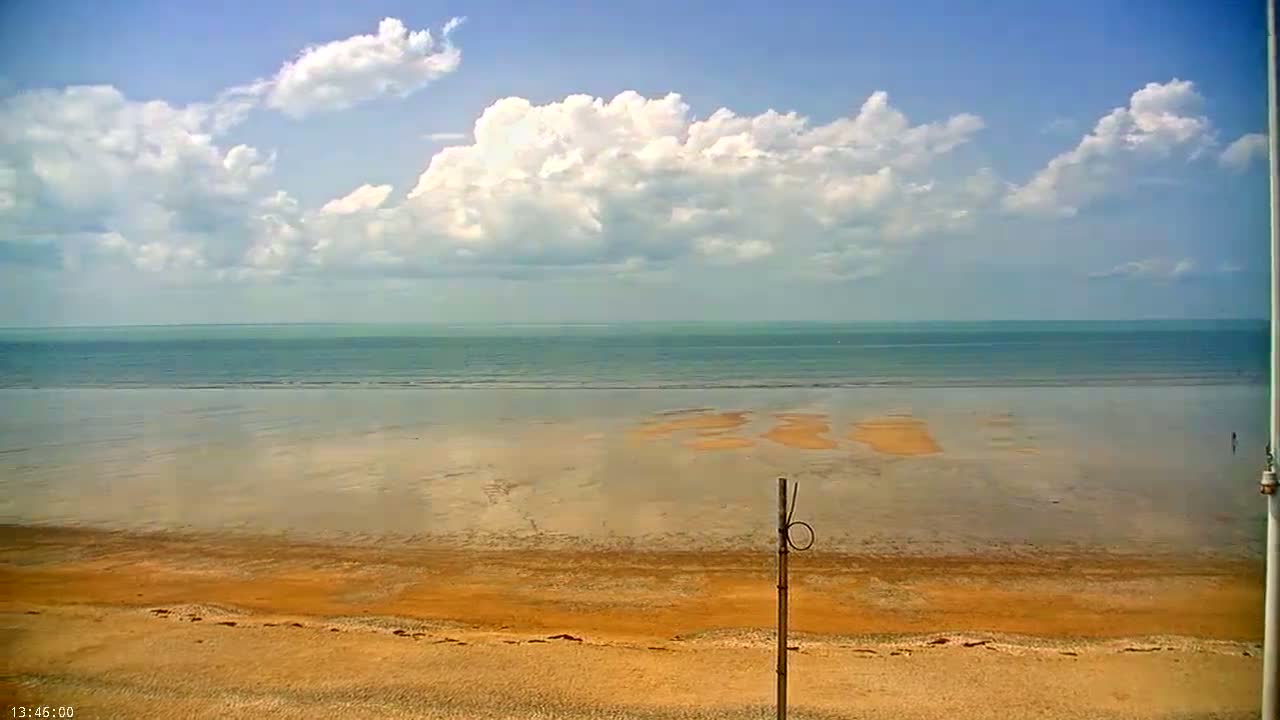 A mostly sunny day at the beach shows a calm sea, a wide expanse of wet sand, and a sandy shore.