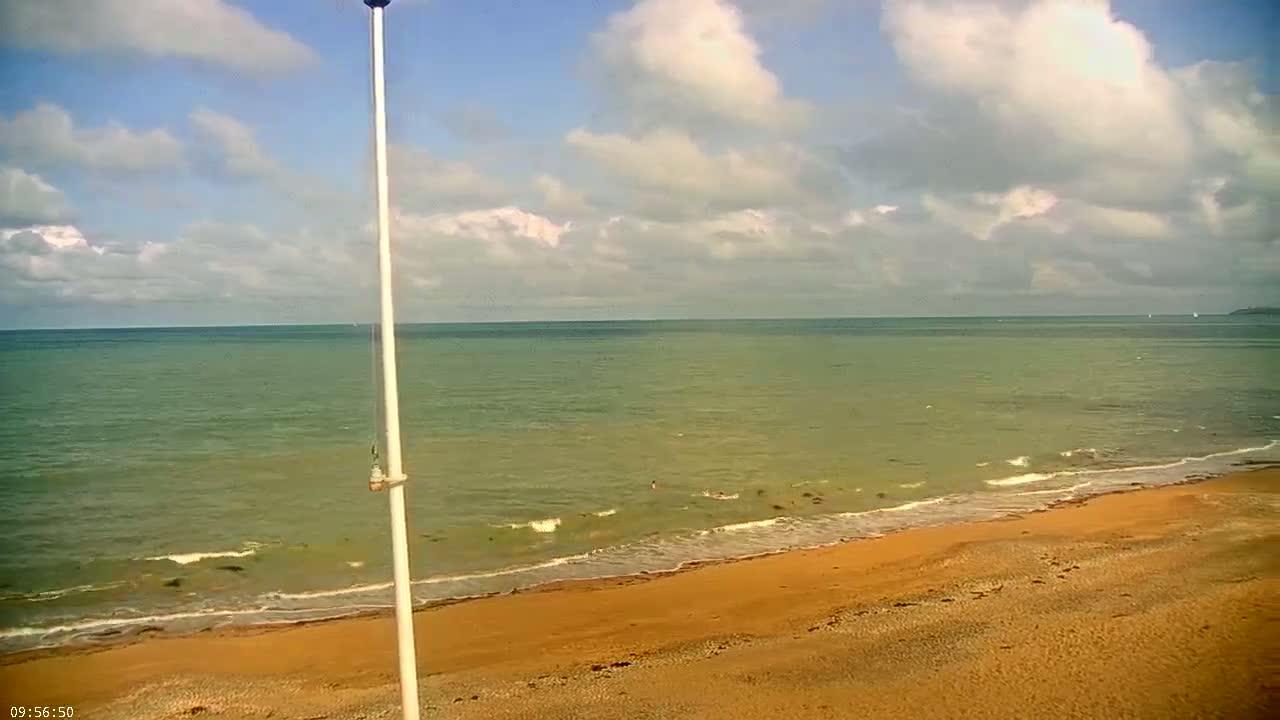 A sandy beach meets a calm, greenish-blue ocean under a partly cloudy sky.