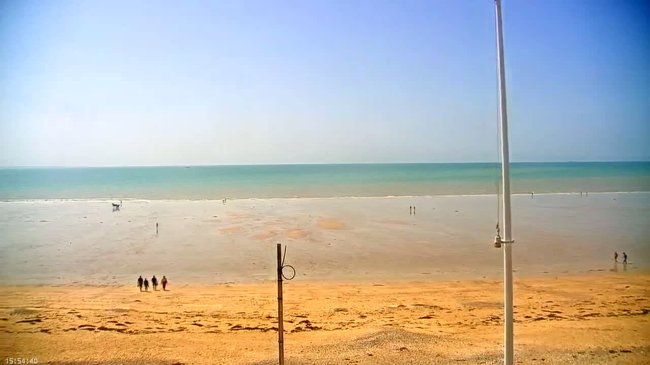 A wide sandy beach stretches out to a calm, teal ocean under a clear blue sky.