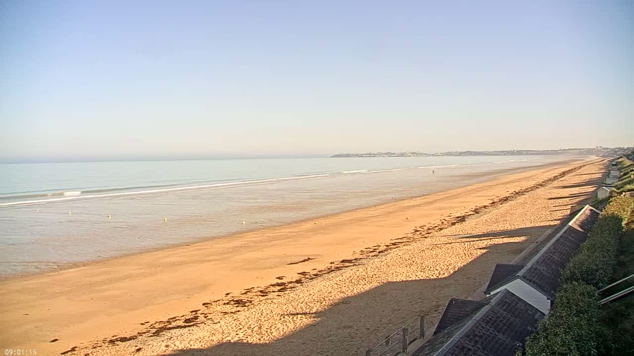 A long, sandy beach stretches to a calm ocean under a clear, bright sky.