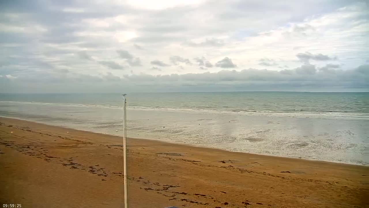 A wide sandy beach stretches to a calm, gray-toned sea under a mostly cloudy sky.