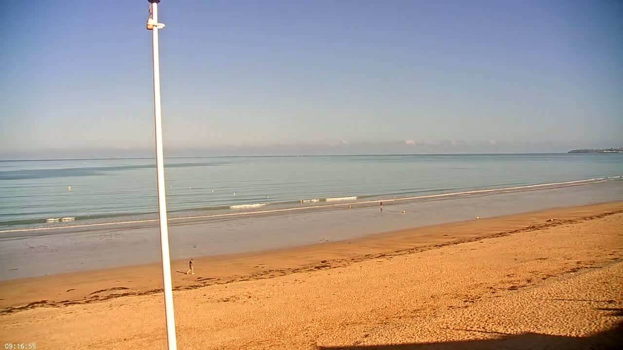 A sandy beach slopes down to a calm ocean under a clear blue sky.