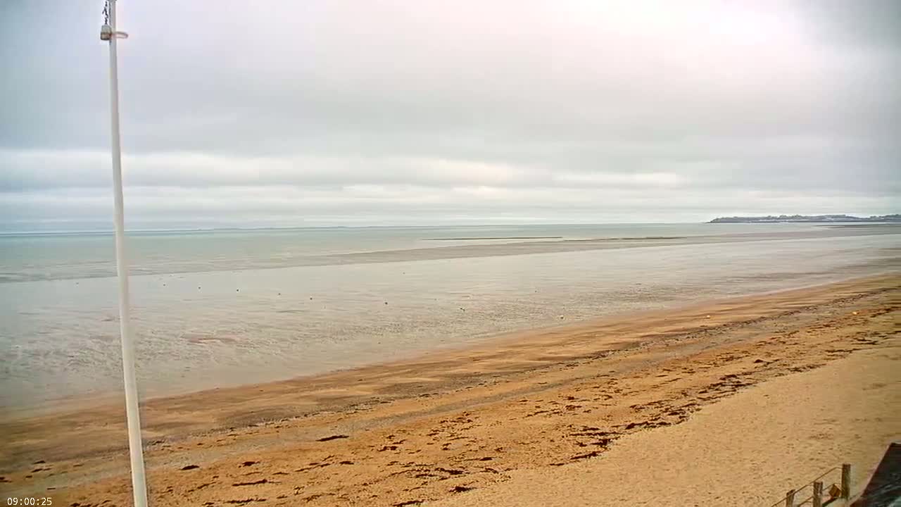 A wide sandy beach stretches to a calm, shallow ocean under a cloudy sky.