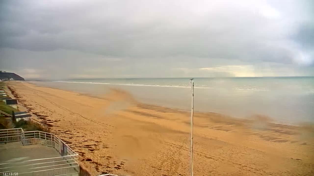 A group of people are exercising on a sandy beach under a partly cloudy sky, with calm ocean waters in the background.