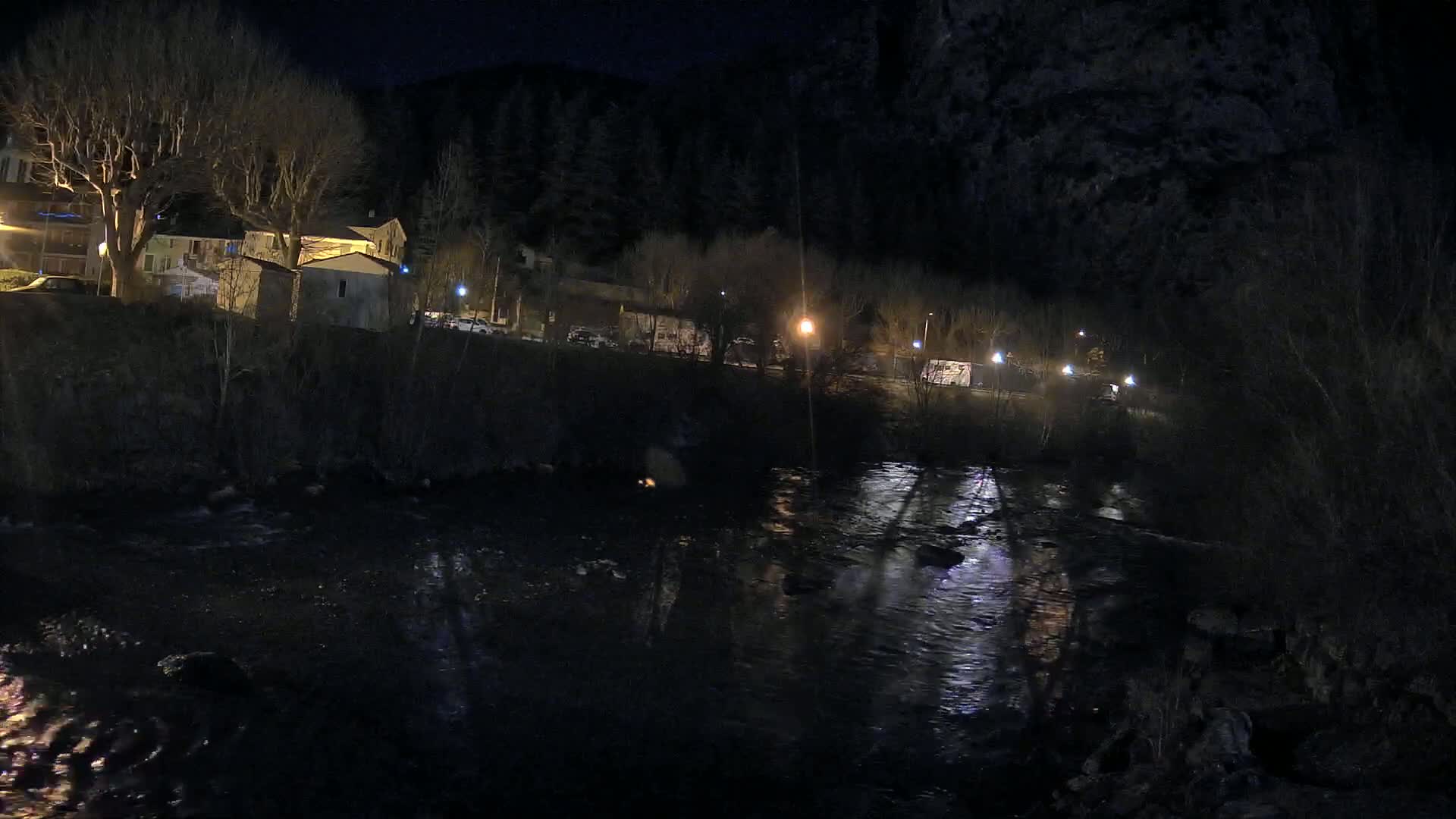 A dark river flows past a small town at night, illuminated by scattered streetlights.