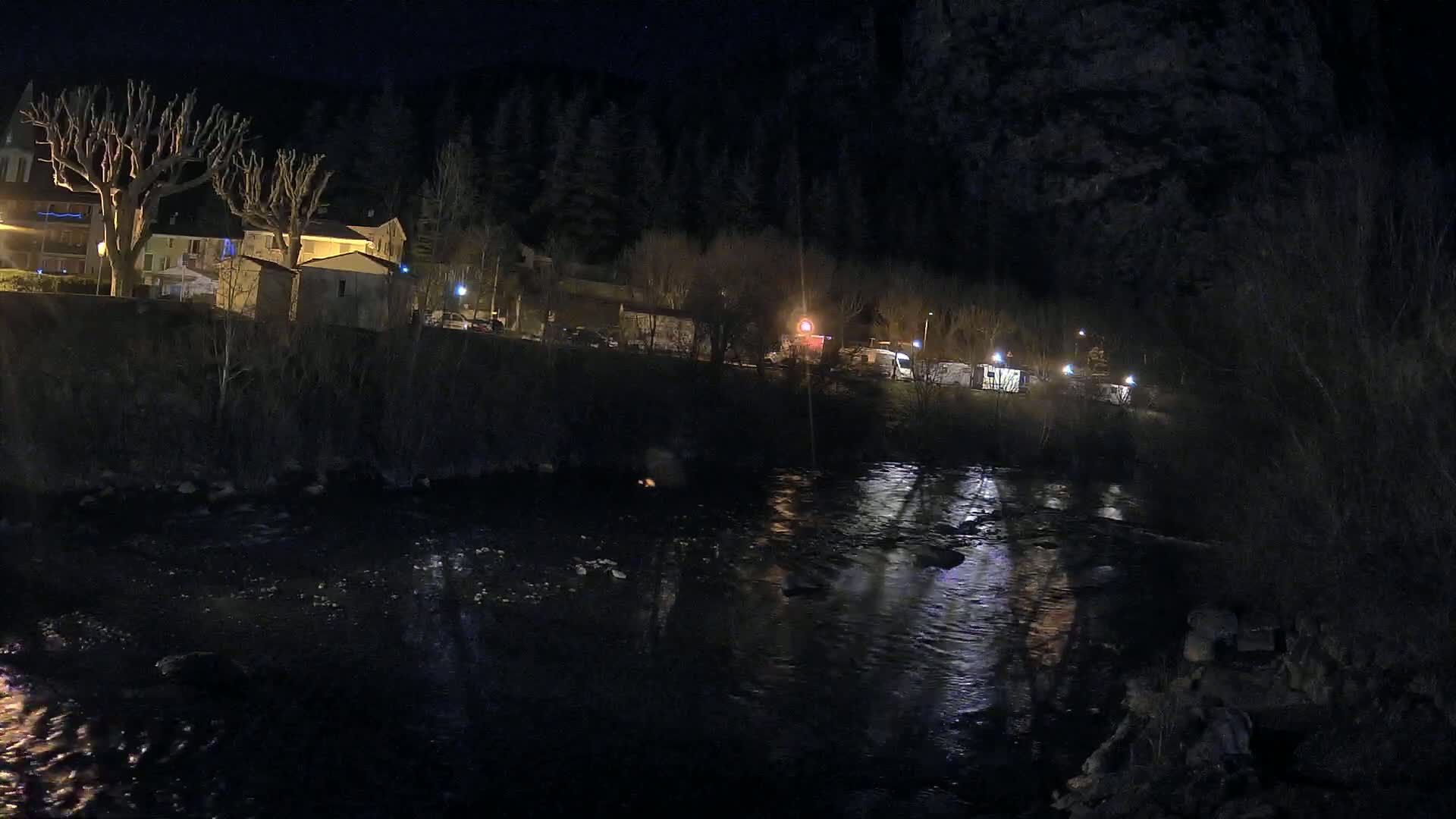 A dark river reflects the lights of a small village at night under a clear, starlit sky.