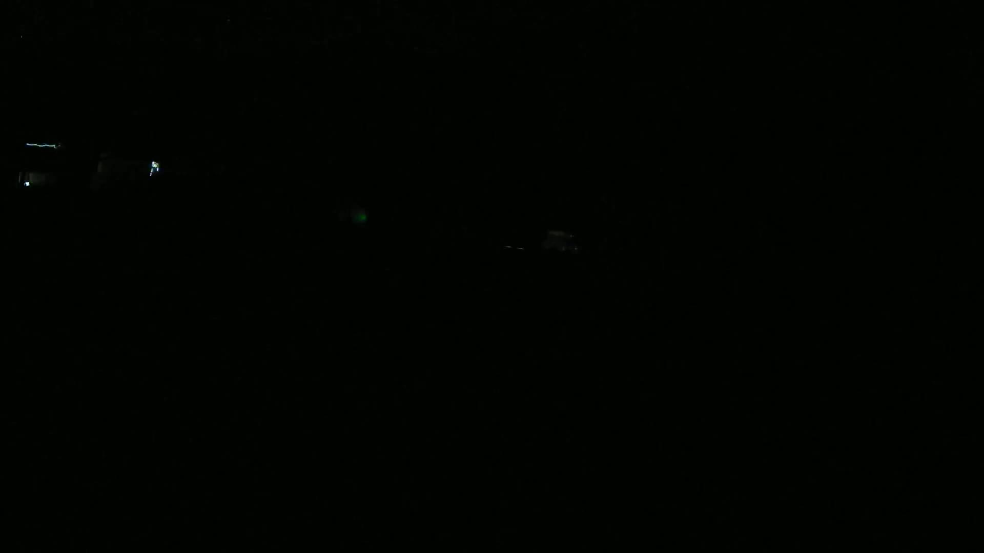 A very dark, nighttime scene shows a few faint lights in the distance.