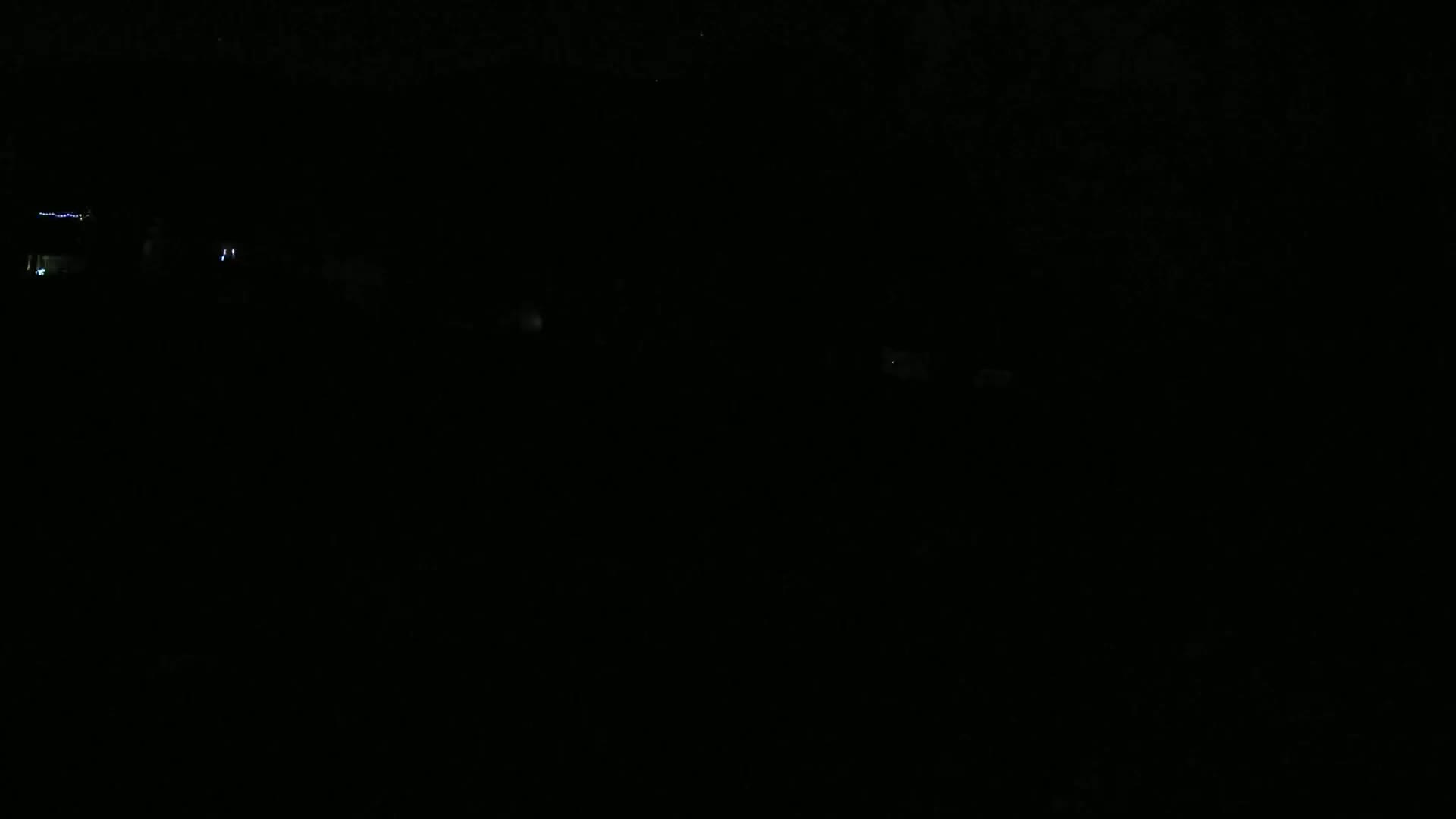 A very dark nighttime scene shows a few faint lights in the distance.