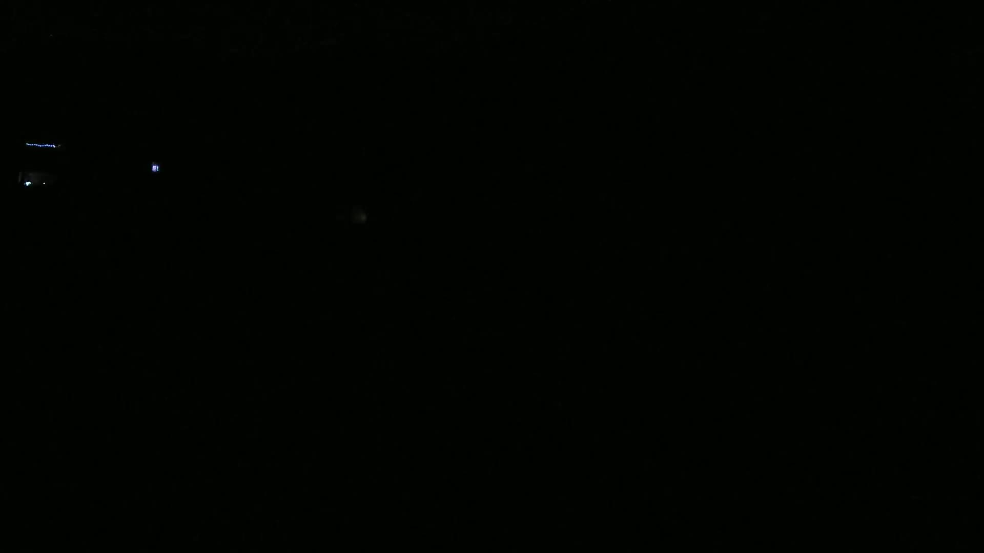 A dark, nighttime scene shows a few faint lights in the distance.