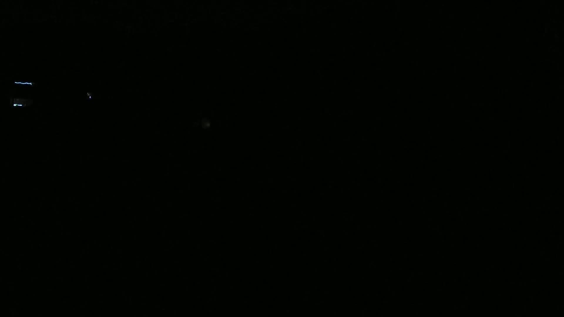 A mostly dark image shows a few faint lights and what appears to be a lightning strike in the distance at night.