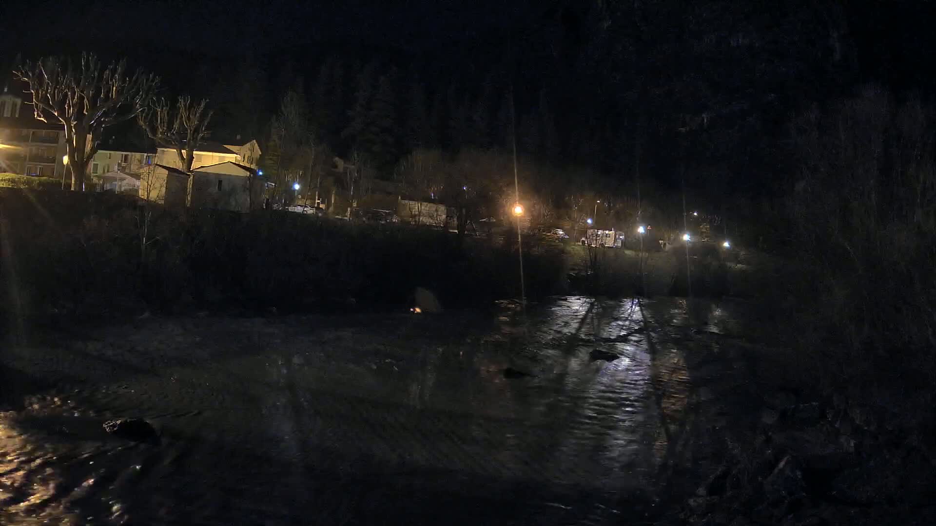 At night, a flowing river reflects the lights from buildings and vehicles along its banks.