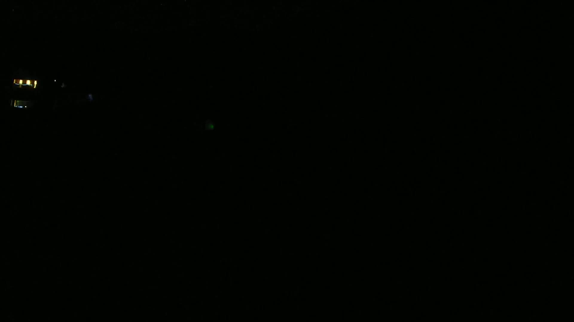 A very dark, nighttime scene shows a few faint lights in the distance.