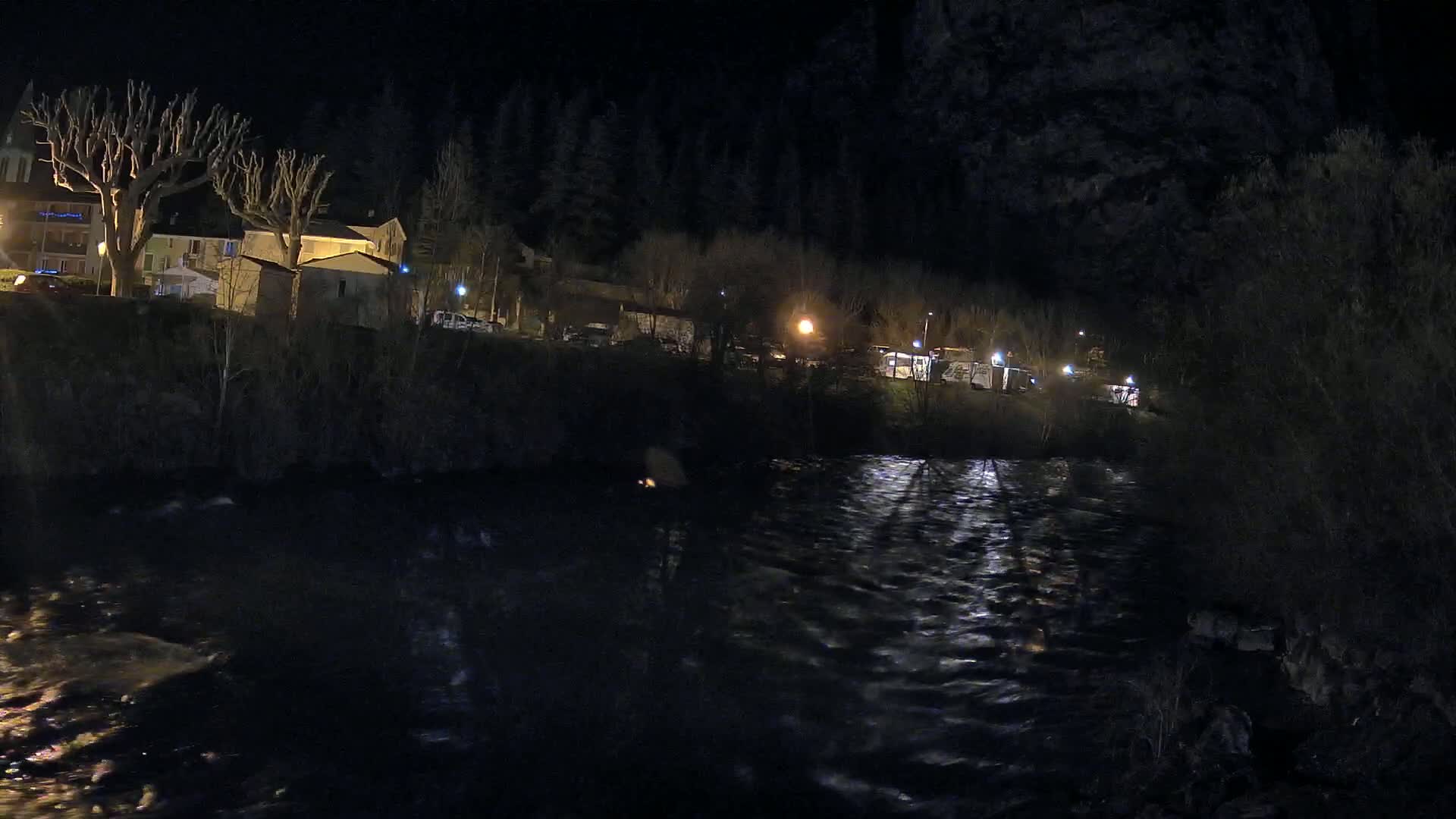 A dark river flows past a small village at night, illuminated by streetlights.