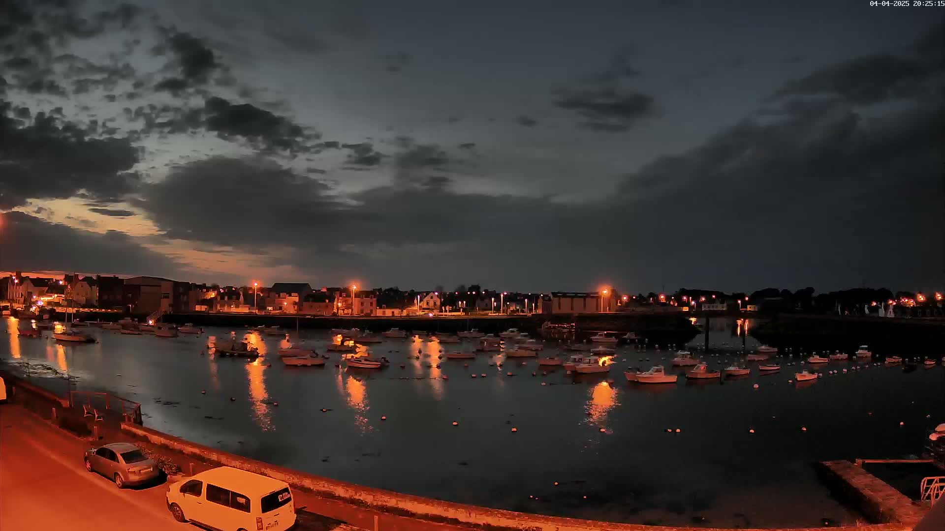 A harbor filled with boats is illuminated at night under a partly cloudy sky.