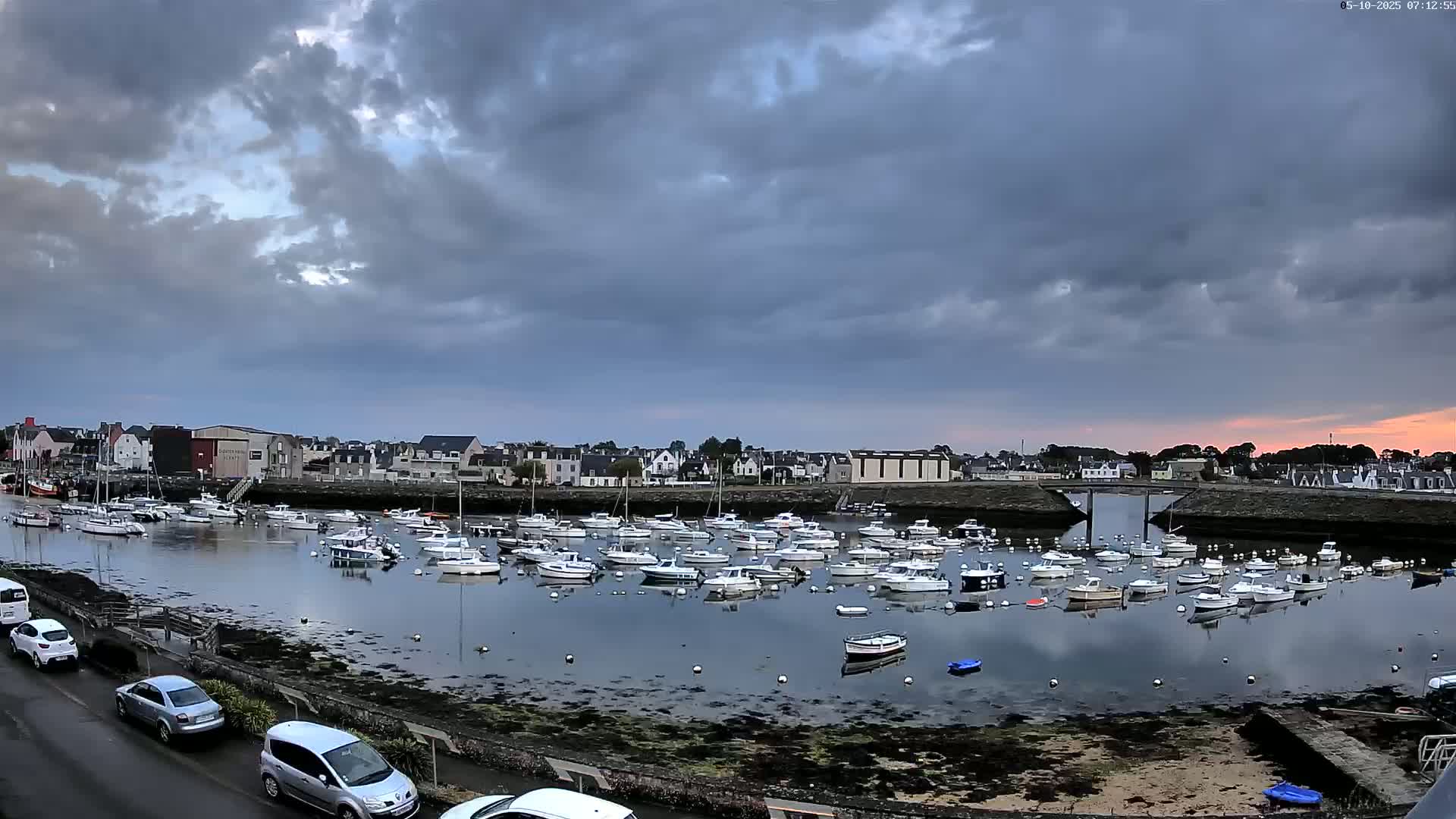 A harbor filled with numerous small boats is seen under a cloudy sky with a hint of sunset.