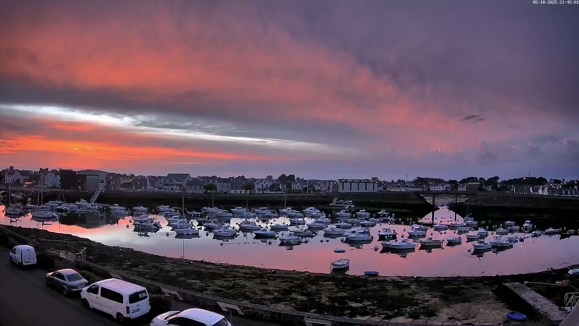 Many boats are docked in a calm harbor at sunset under a pink and purple sky.