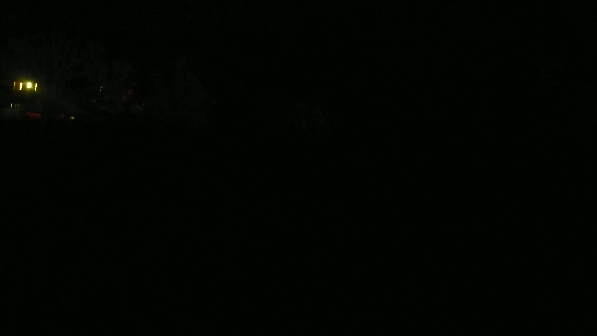 A dimly lit nighttime scene shows a building with illuminated windows partially obscured by trees.