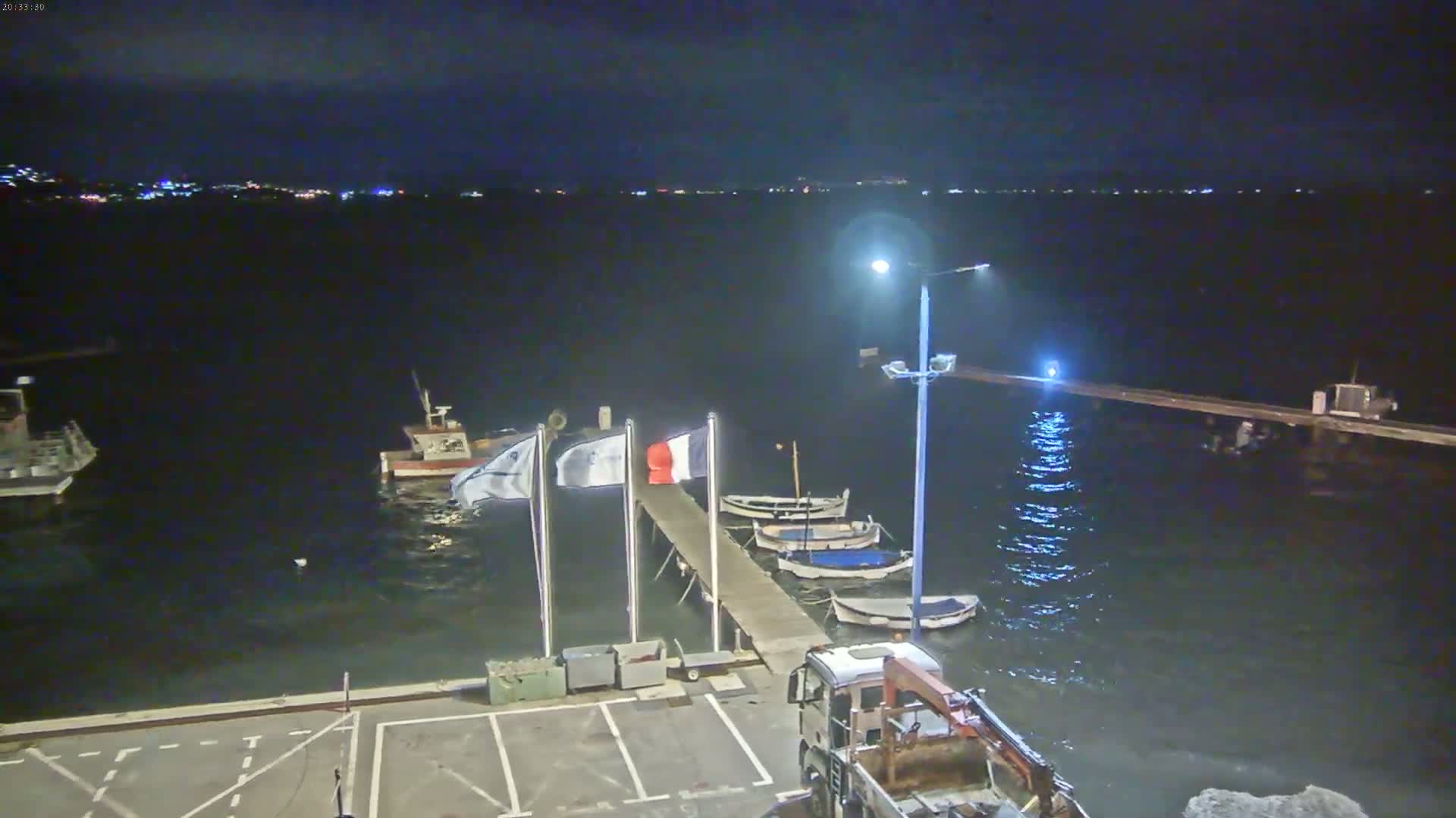 A nighttime view of a harbor with several small boats moored at a pier, under a calm, dark sky.