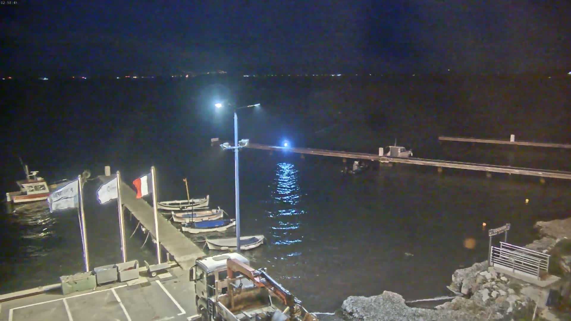 A nighttime view of a harbor with several small boats moored at a pier under a dark sky.