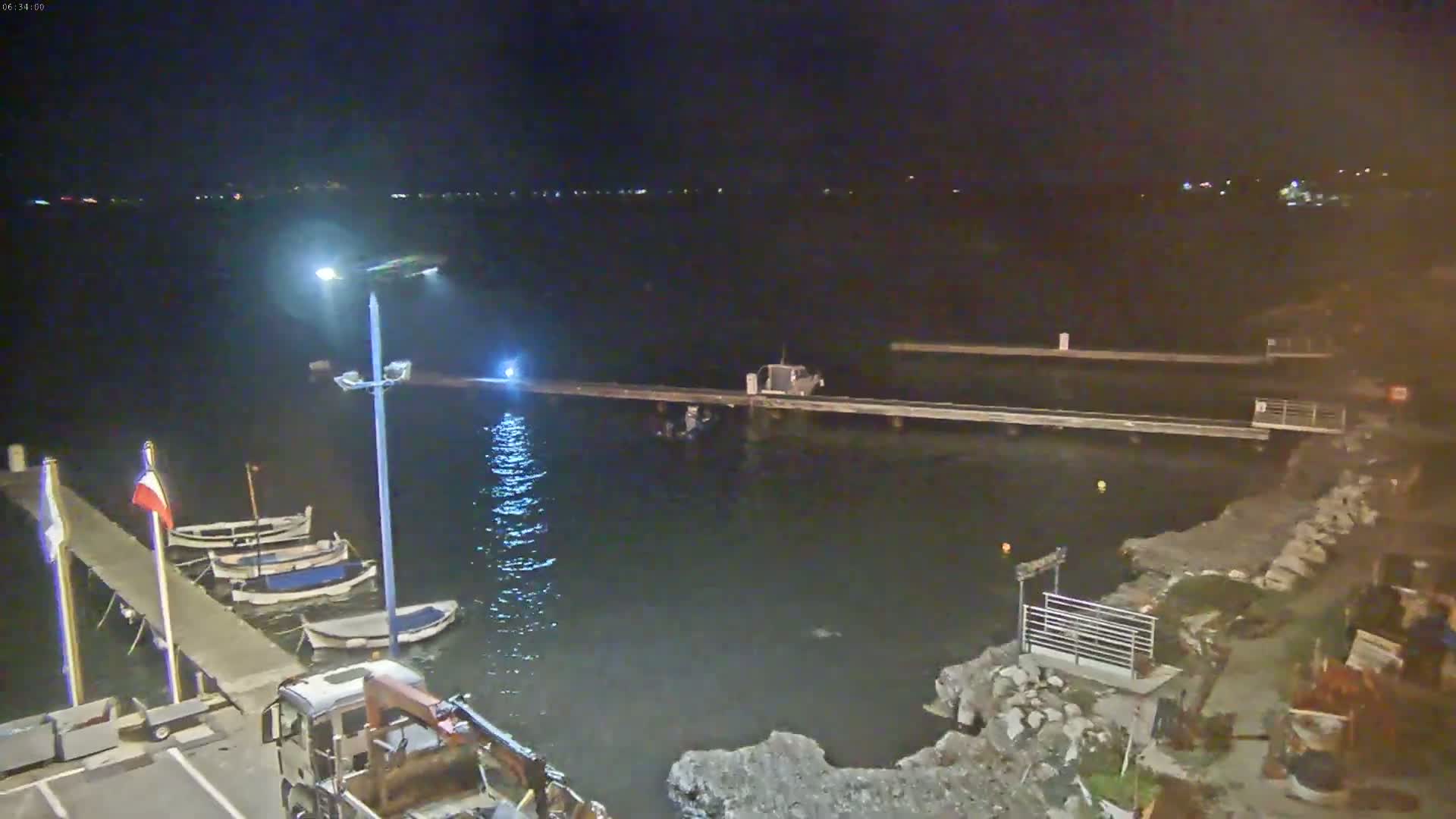 At night, several small boats are moored at a pier next to a body of dark water, with a small truck parked nearby.