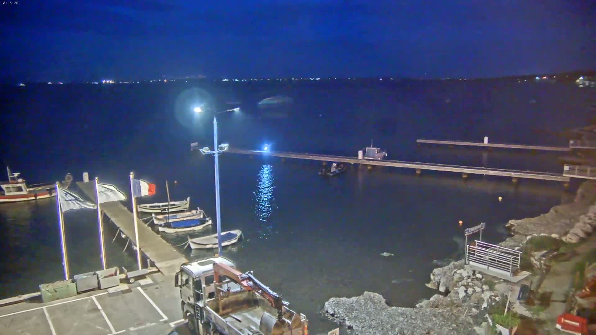 Several small boats are moored at a pier at night under a dark, clear sky, with a larger truck parked nearby.