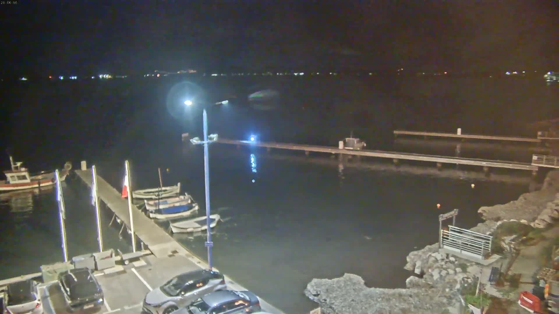 A nighttime view of a harbor with several small boats moored at a dock, under a clear, dark sky.