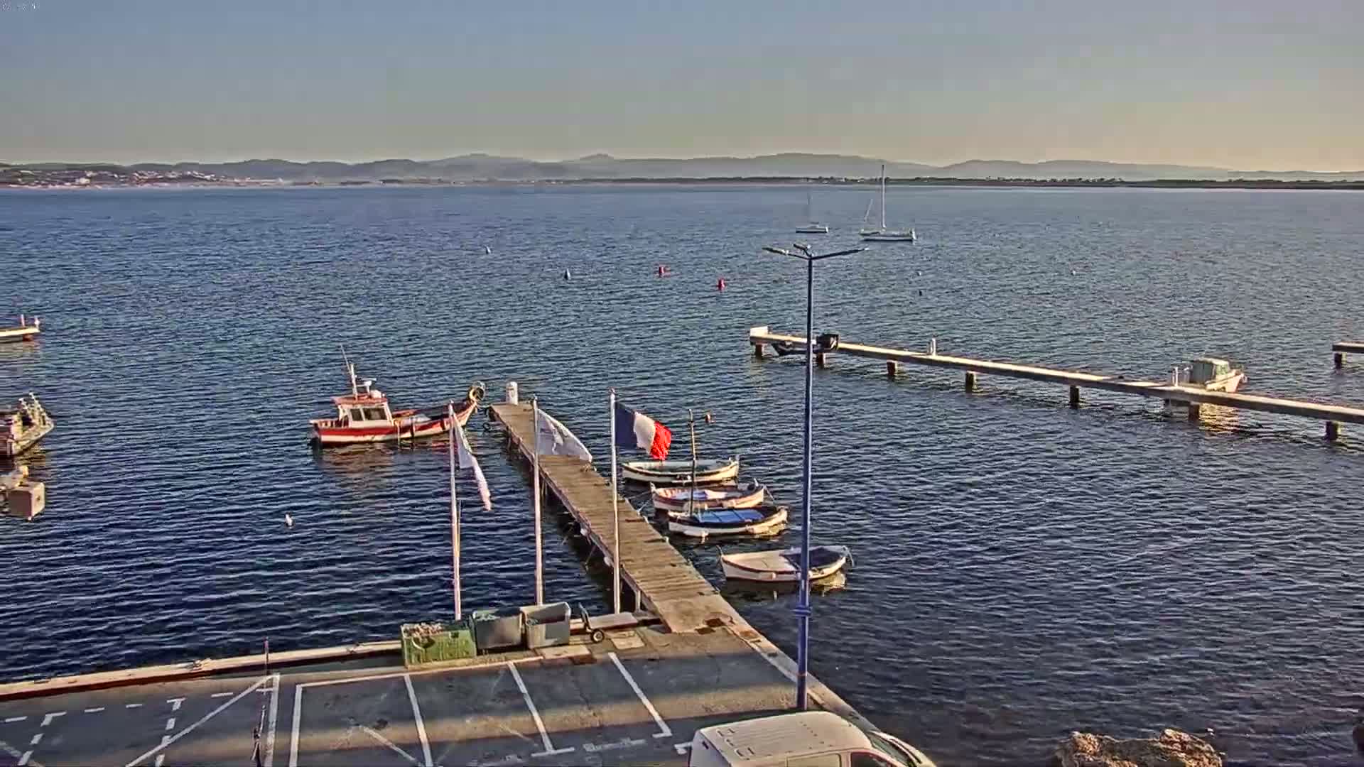 A calm body of water with several small boats moored at a wooden pier, under a clear sky.