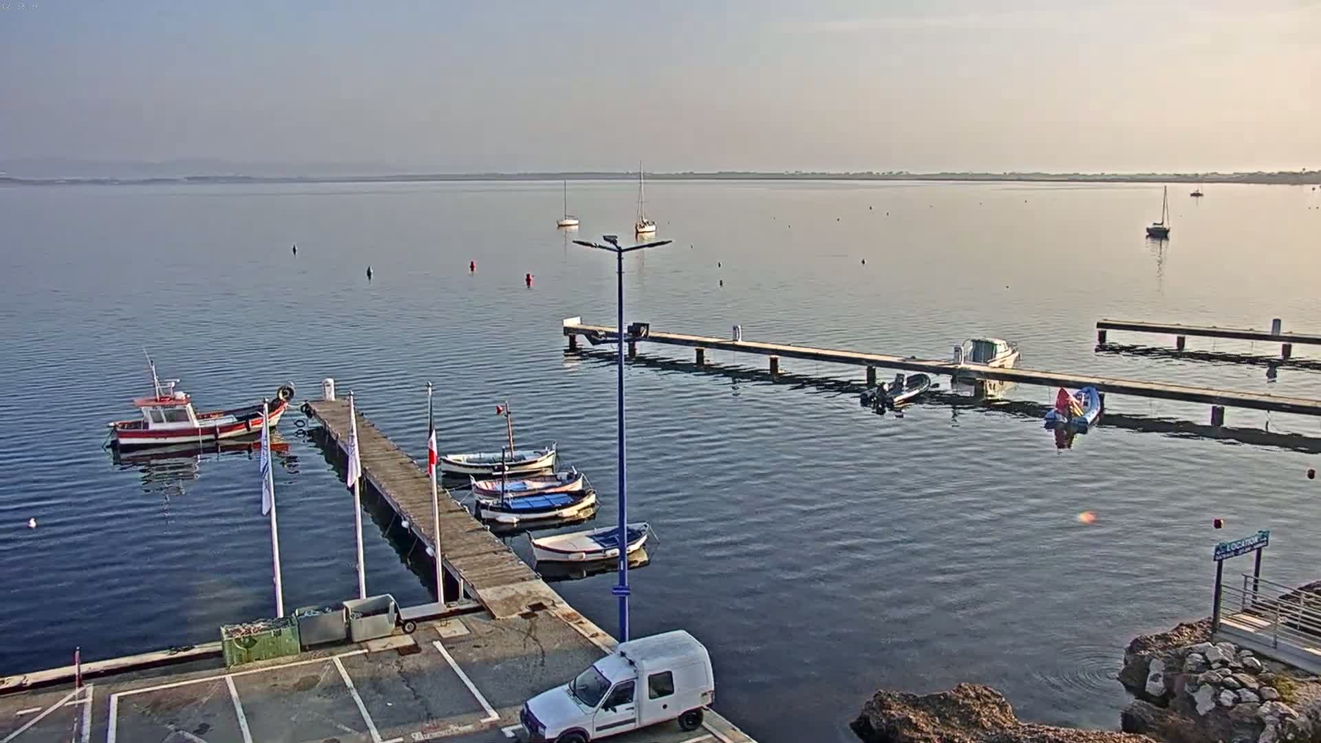 Several small boats are moored at wooden docks in a calm body of water under a clear, bright sky.