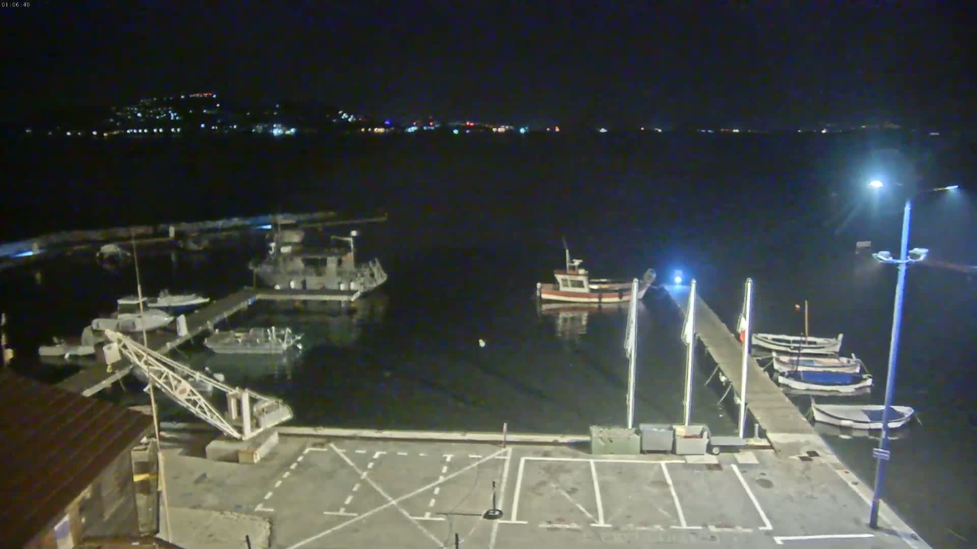 A nighttime view of a harbor with several boats docked, a crane, and a pier, under clear skies.