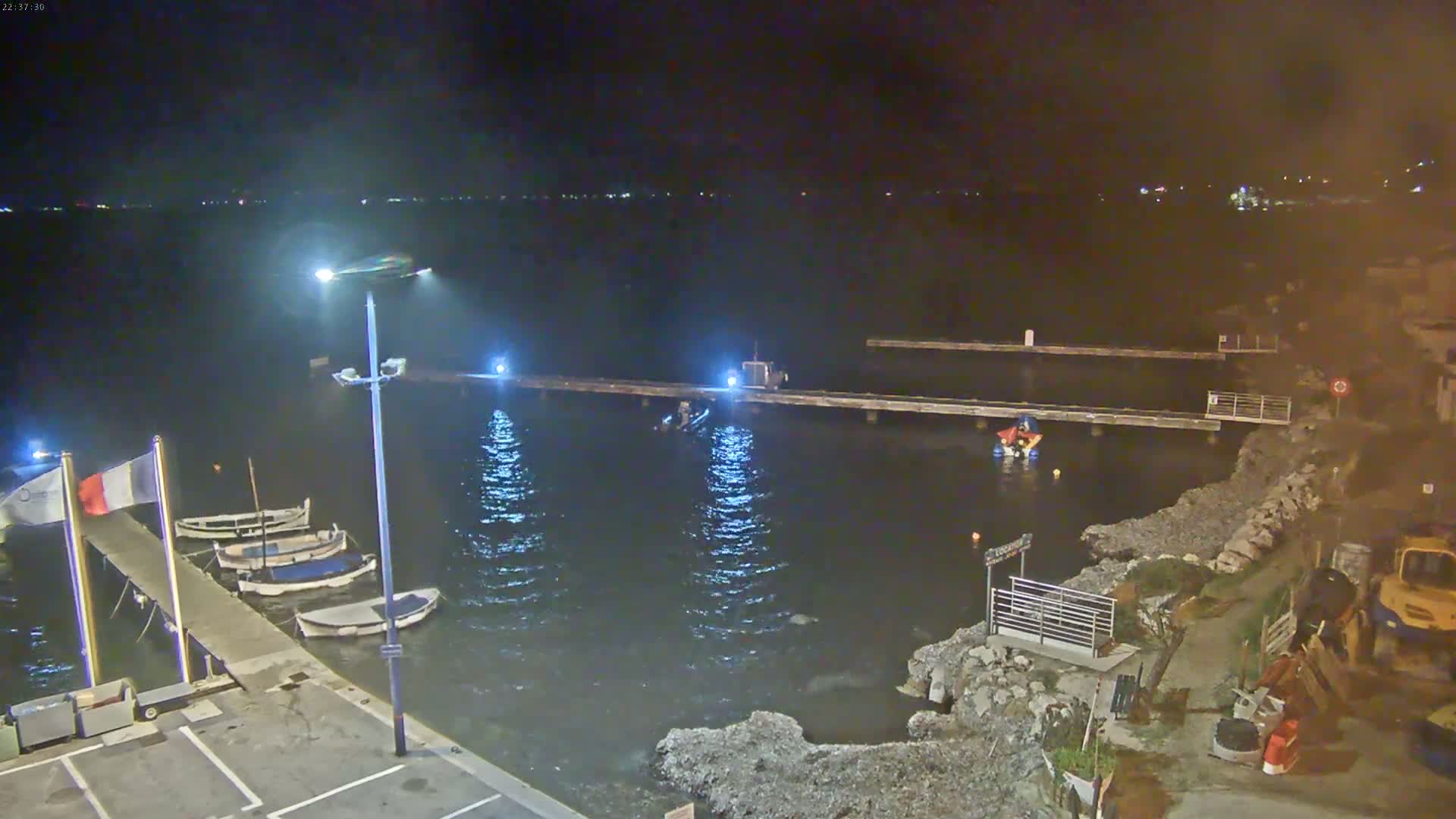A nighttime view of a small harbor with several boats docked at a pier, under calm water conditions.
