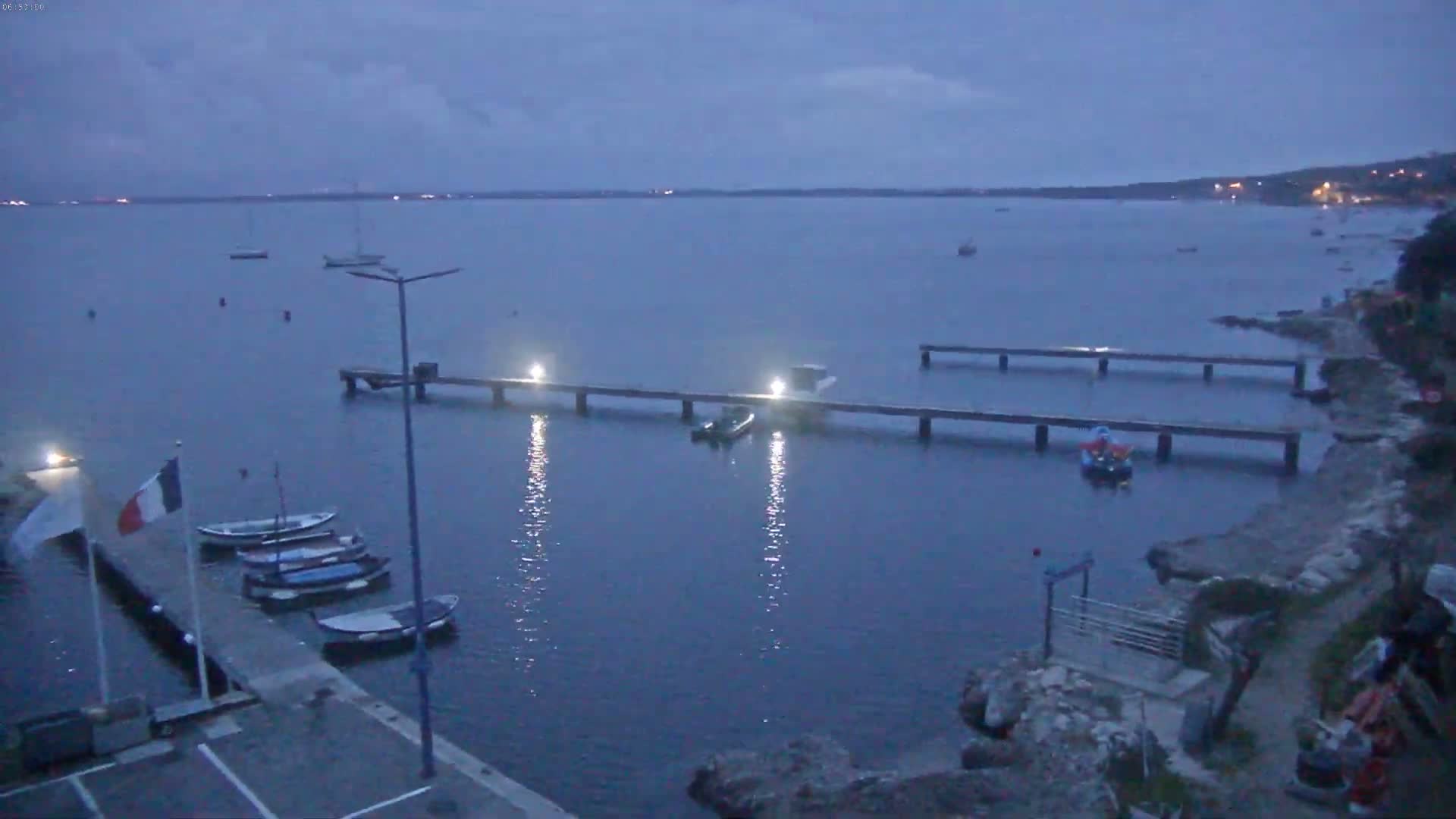 Several boats are moored at a pier and in the calm waters of a bay under a twilight sky.
