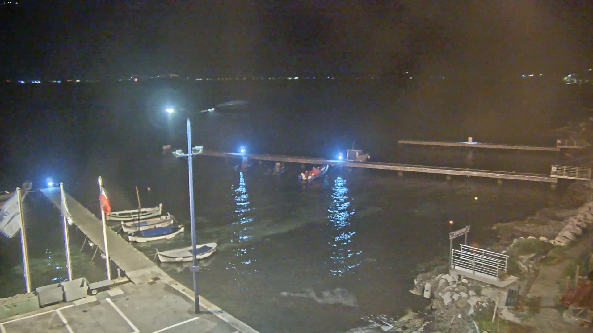 At night, several small boats are moored at a pier next to a body of dark water under a clear, dark sky.