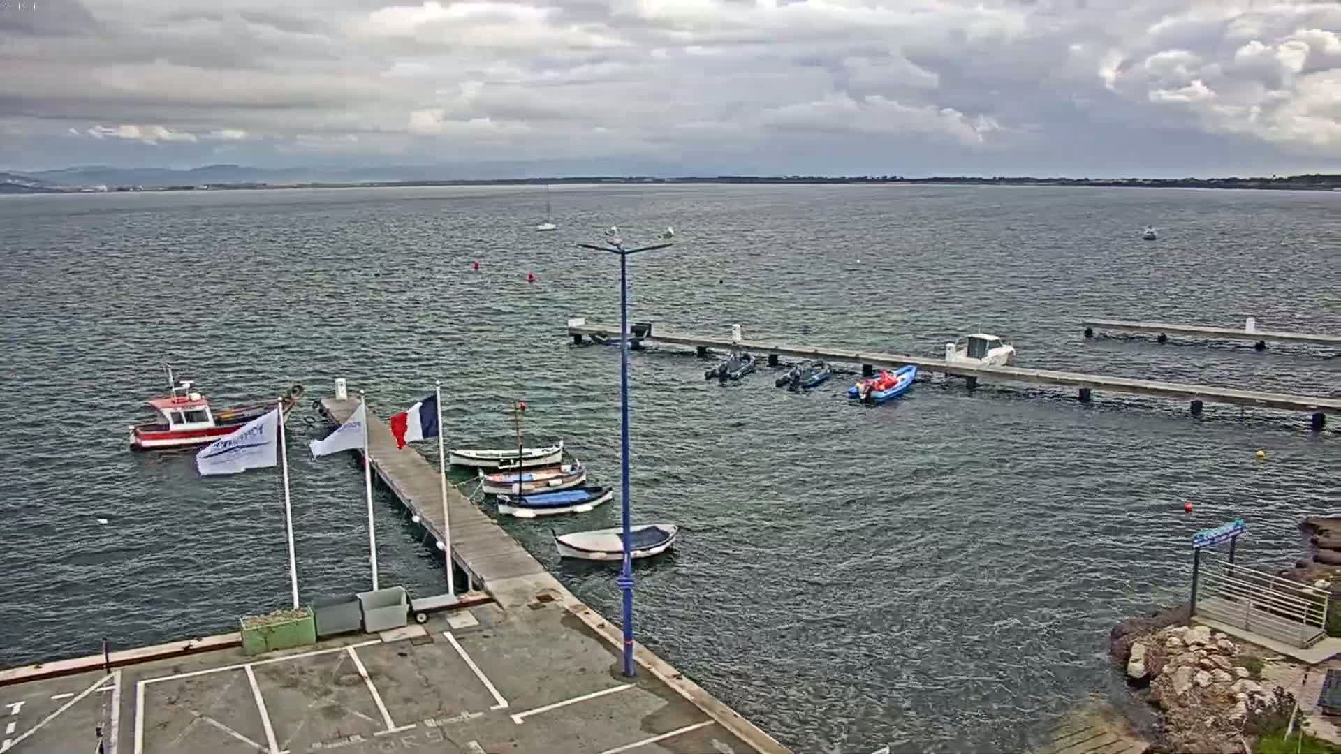 Several small boats are moored at a pier on a calm body of water under a cloudy sky.