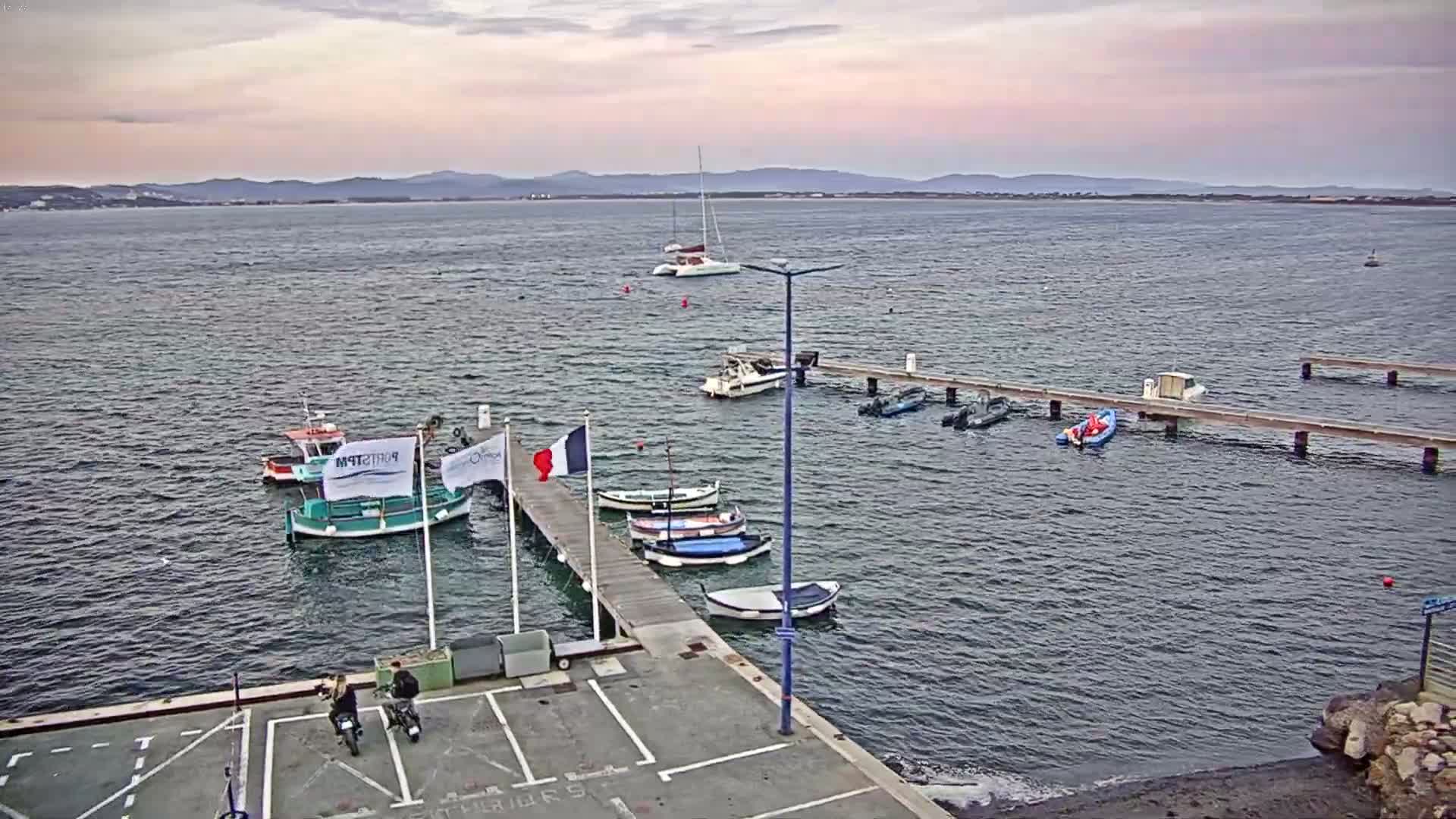 A calm body of water with several boats docked at a pier, under an overcast sky.