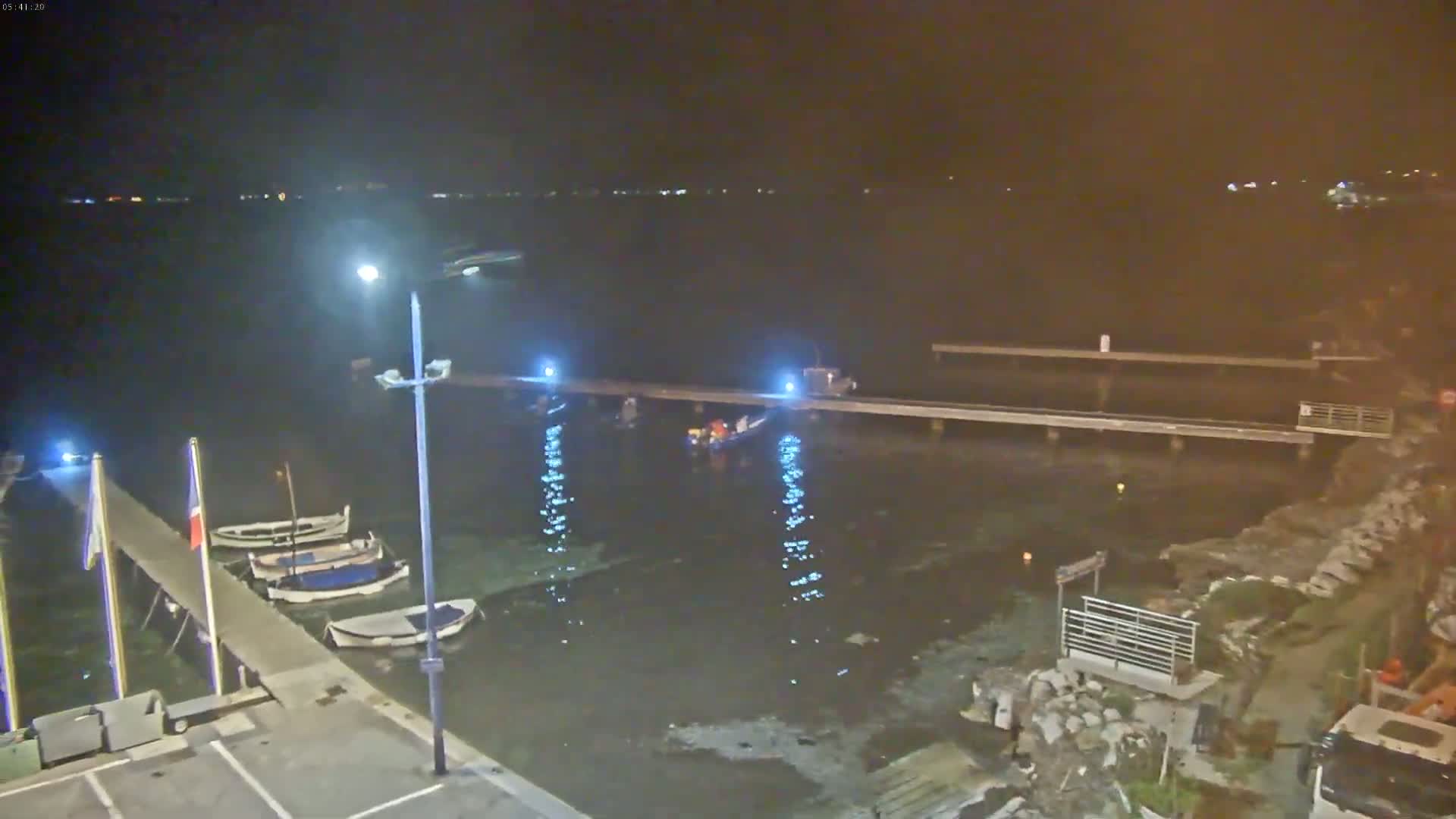 At night, several small boats are moored at a pier next to a body of dark water, with a group of people gathered near a boat in the water.