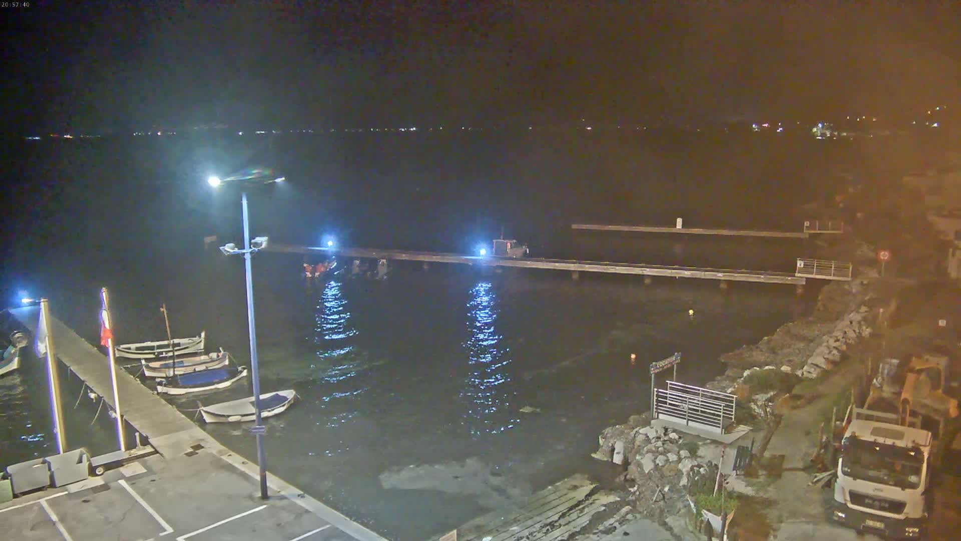 A nighttime view of a harbor with several small boats moored at a pier, under calm water conditions.