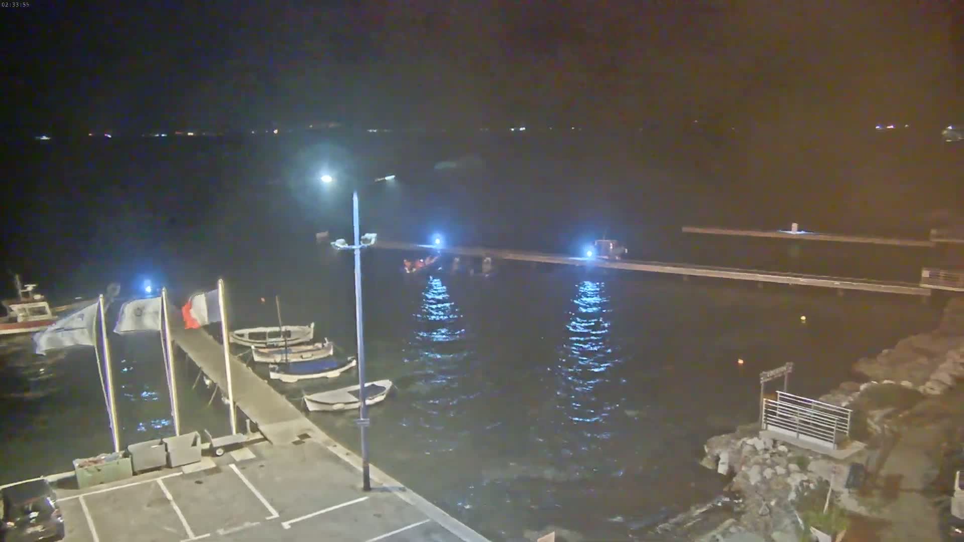A nighttime view of a harbor with several small boats moored at a pier, under calm, dark conditions.
