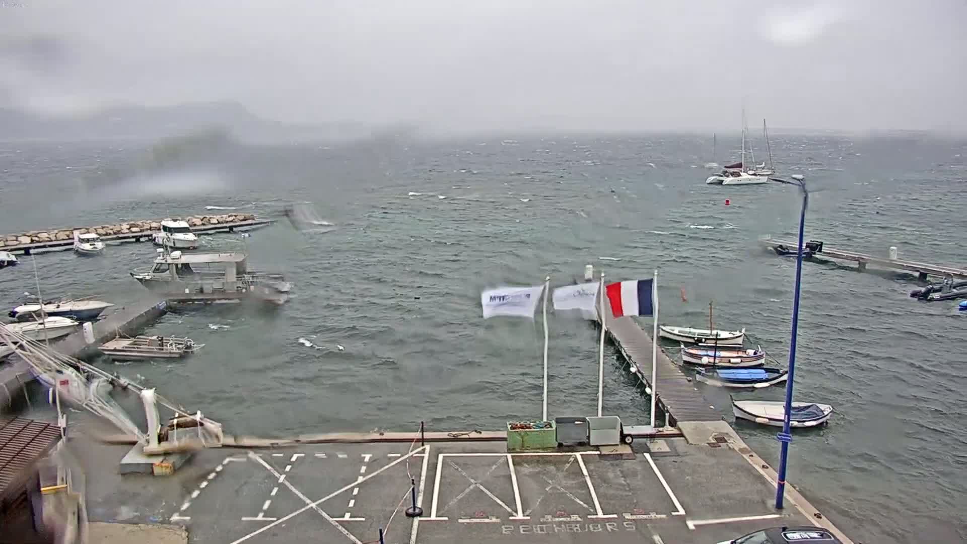 A marina with numerous boats is shown under stormy conditions with choppy water and a gray sky.