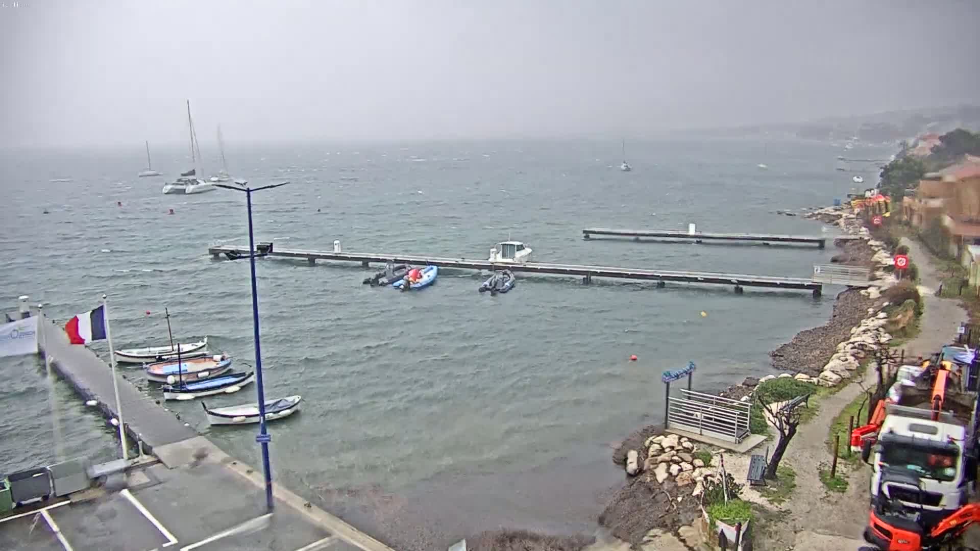 Several boats are moored at docks along a rocky shoreline on a windy, overcast day.