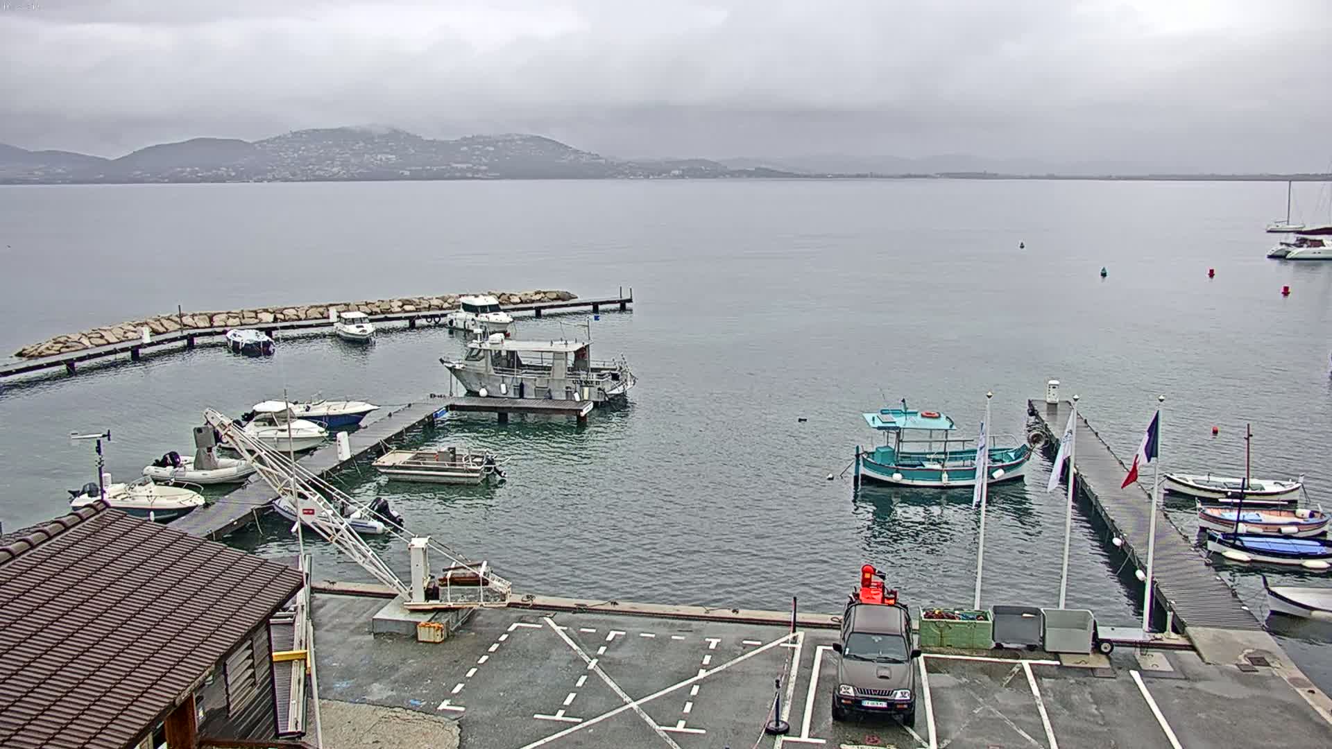 A small harbor filled with boats on a cloudy day, with mountains visible in the distance.