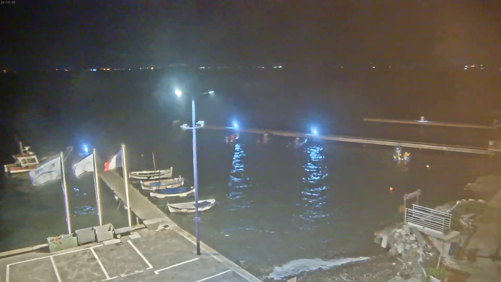 A nighttime view of a harbor with several small boats moored at a pier, under calm water conditions.