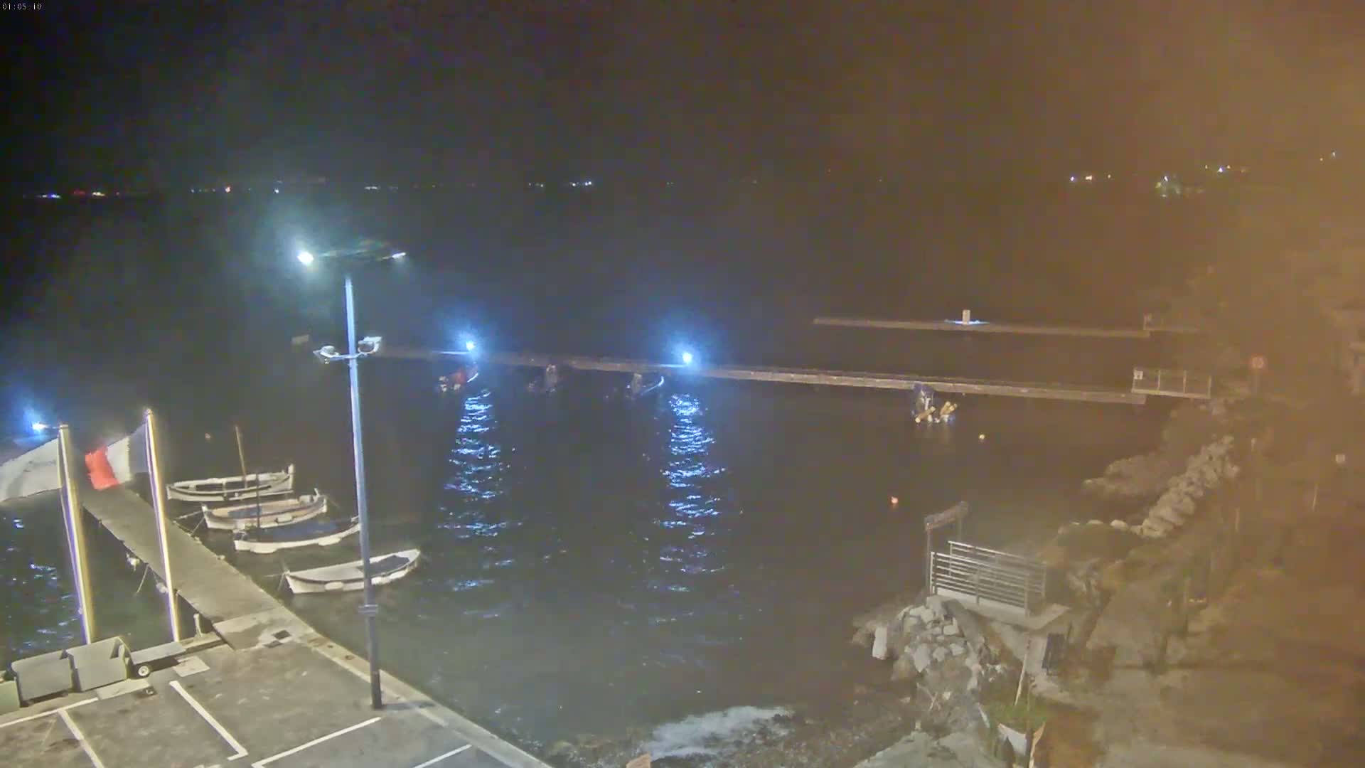 Several small boats are moored at a pier at night, under slightly hazy conditions, with calm, dark water.