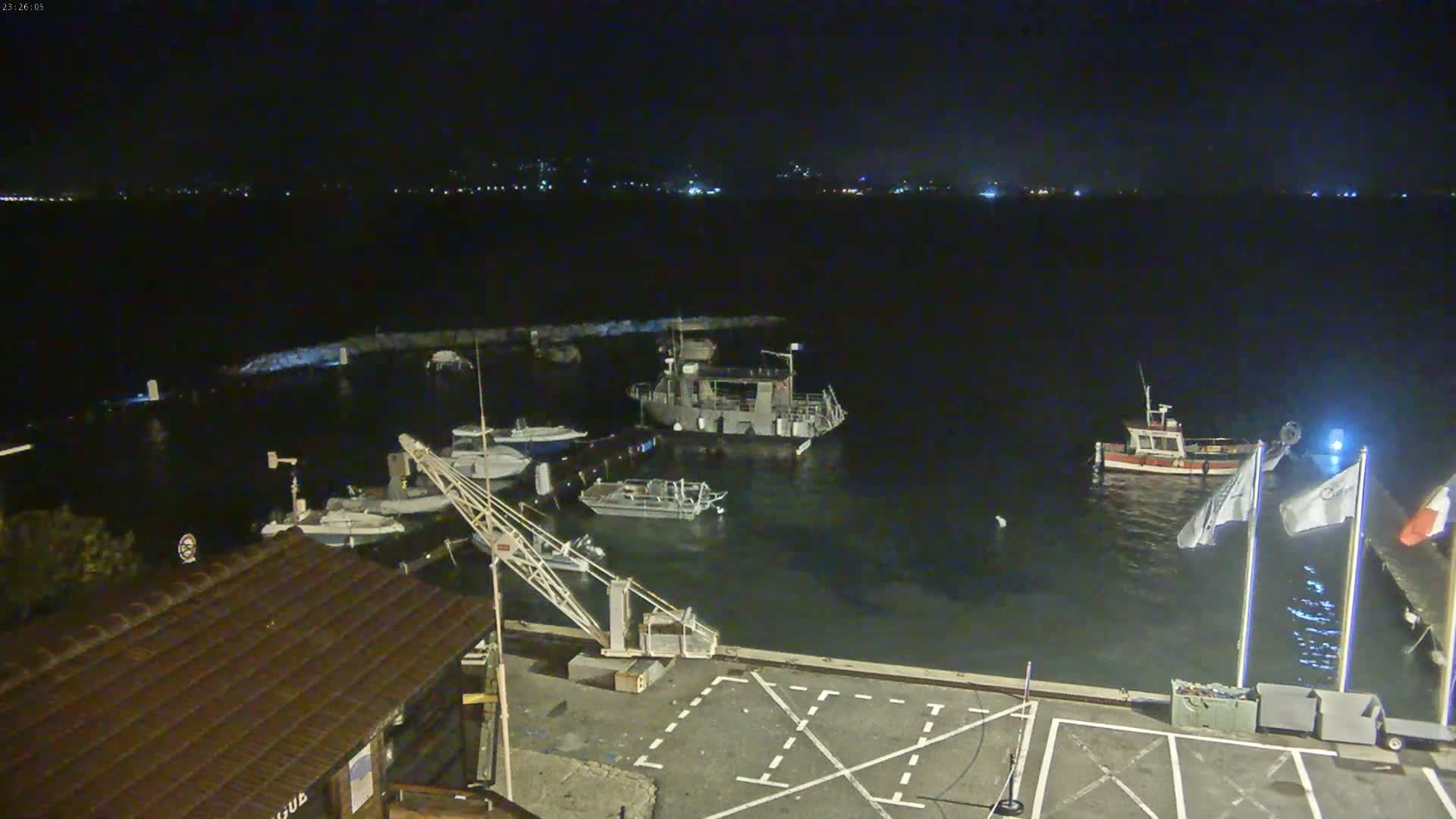 A nighttime view of a harbor with several boats moored, a small crane, and a building under a dark, clear sky.