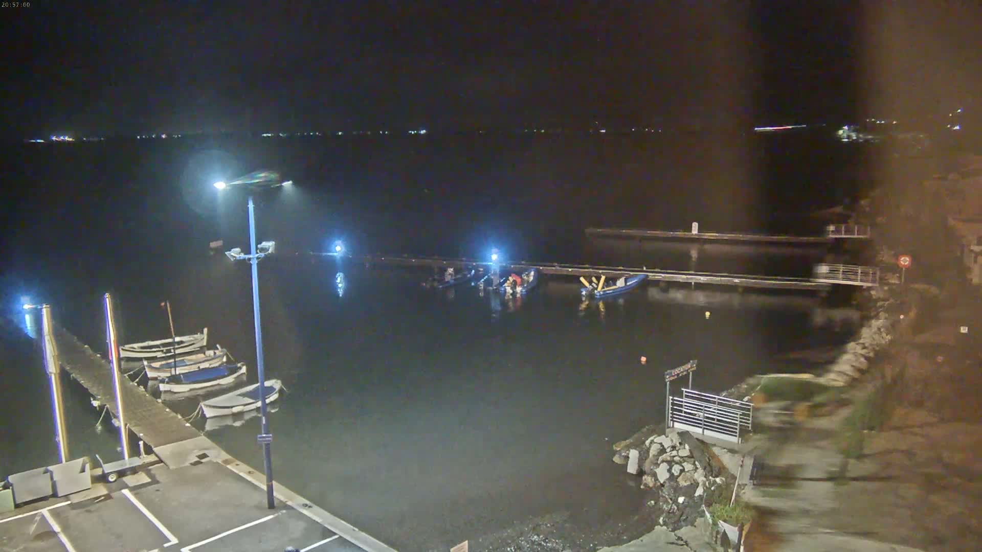 A nighttime view of a calm body of water with several boats docked at a pier, under a dark sky.