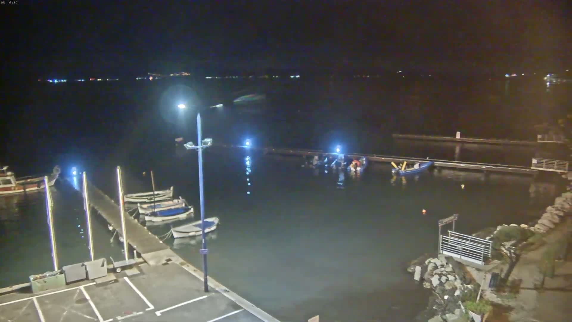 At night, several small boats are moored at a dock in calm water under artificial lights.