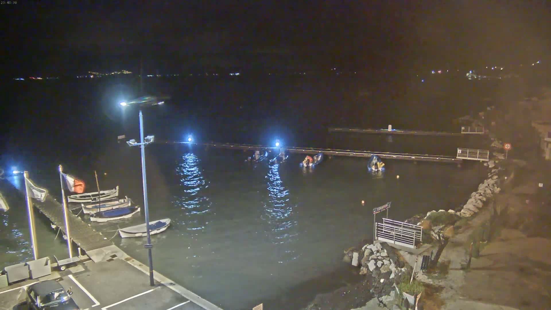 At night, several small boats are moored at a dock on a body of water with gentle waves under partly cloudy skies.