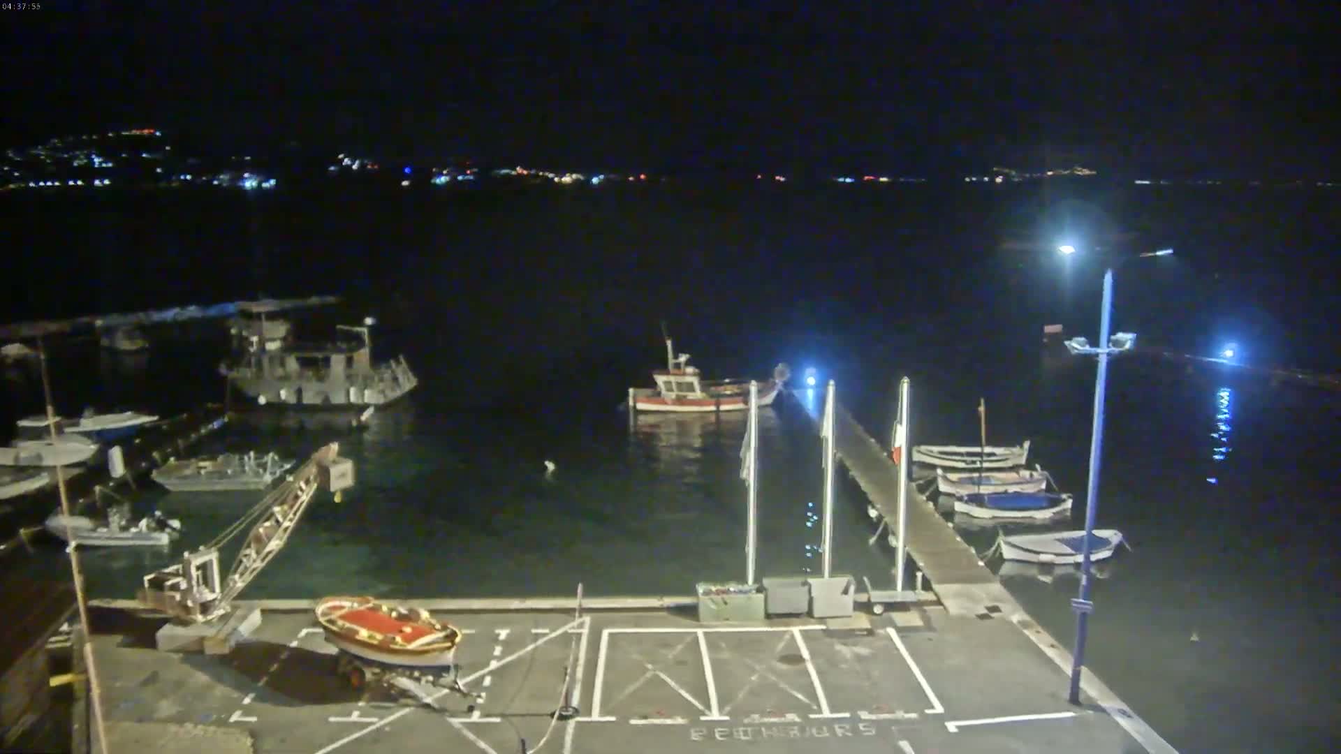 A nighttime view of a harbor with several boats moored at a dock, under a clear, dark sky.