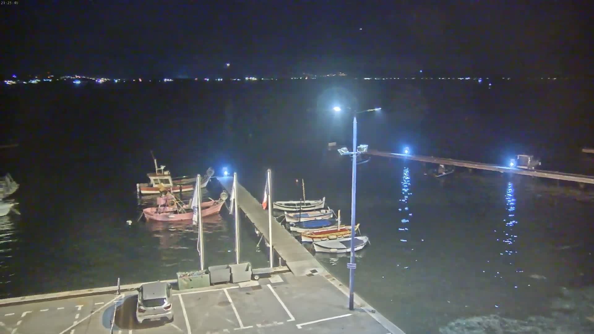 A nighttime view of a small harbor with several boats moored at a pier, under a clear, dark sky.