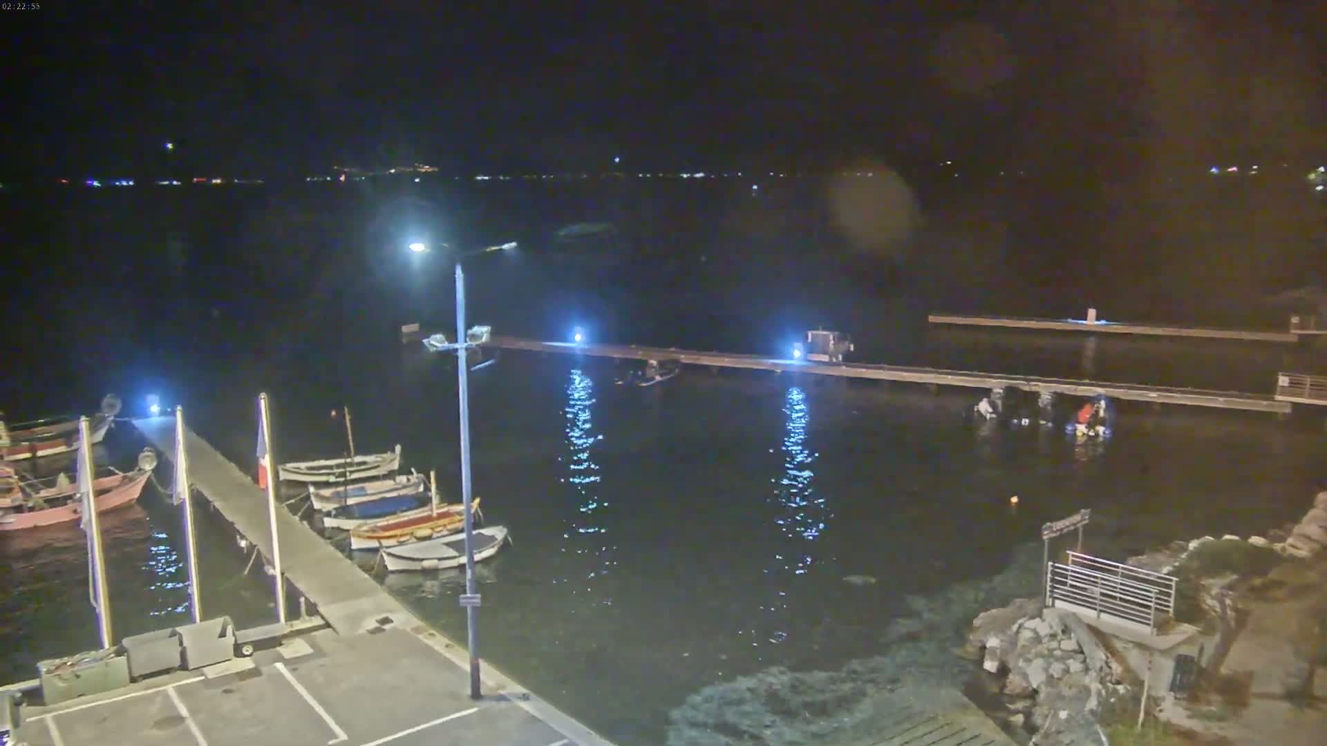 A nighttime view of a calm body of water with several small boats docked at a pier, under a dark sky.